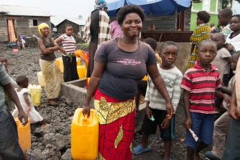 Justine carrying a yellow plastic jerry can from the busy water tap.