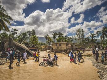 Haitians crossing flooding river in their community
