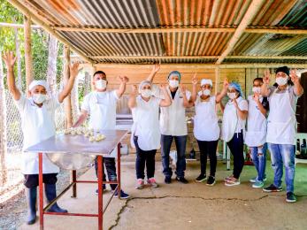 A group of bakers wave at the camera from an outdoor kitchen.
