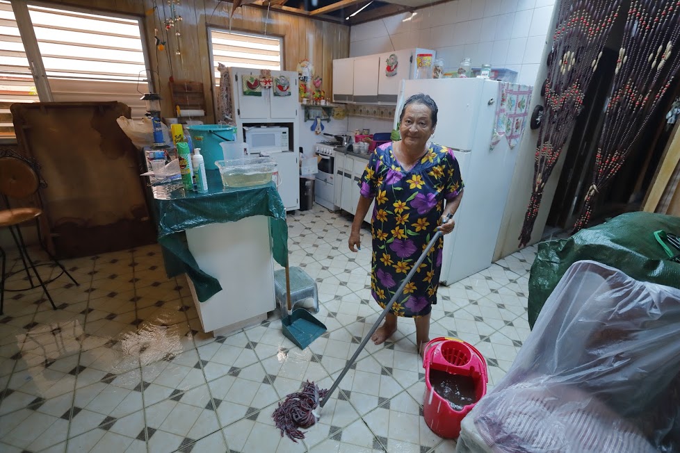 Carmen stands in her kitchen with a mop and bucket