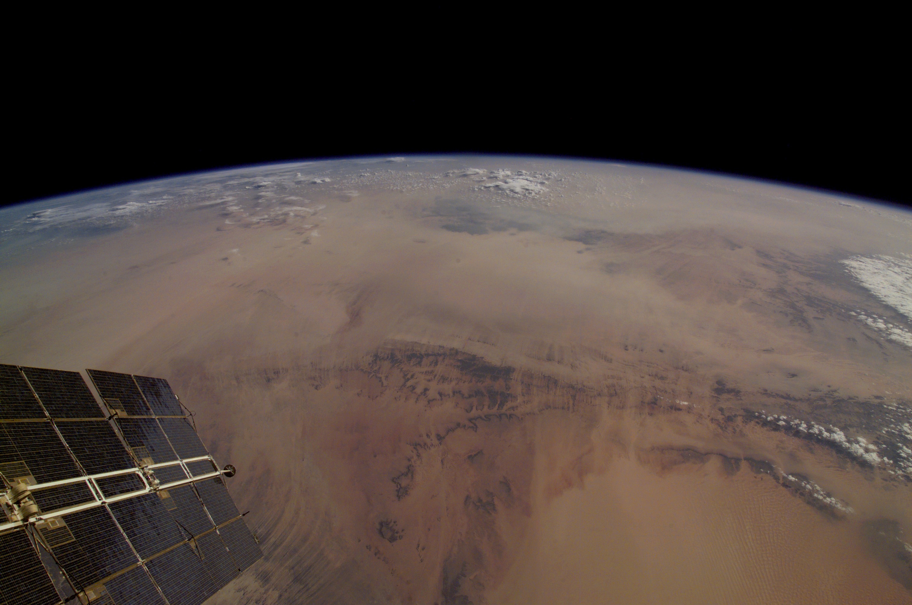 A photo showing a portion of a satellite and the curve of the earth, with the brown Sahara making up the majority of the land shown