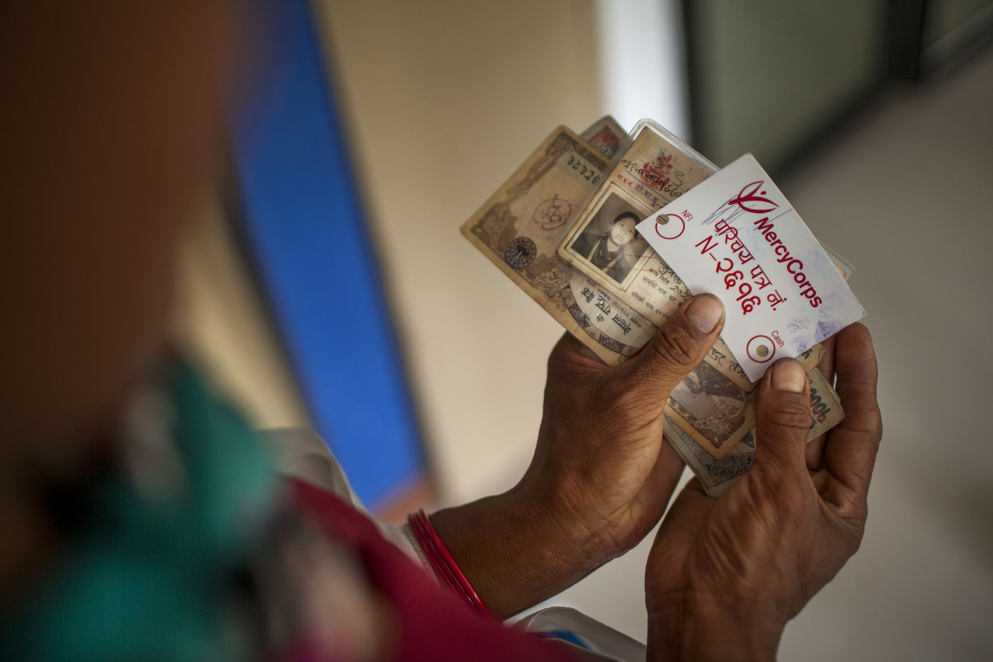 Image: Hands holding cash and a Mercy Corps ID card during a distribution of emergency cash