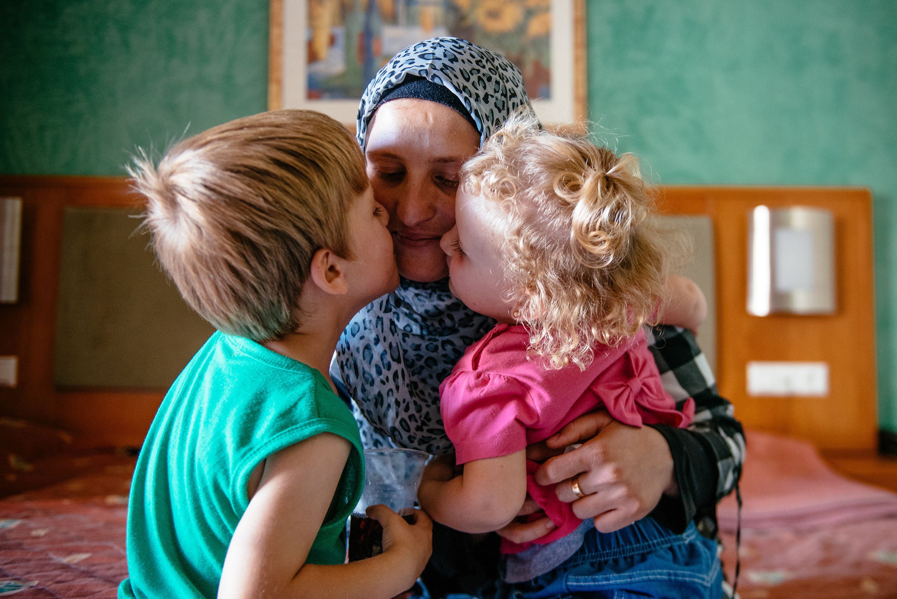 A woman receives kisses on her cheeks from a young boy and girl as she holds them tight