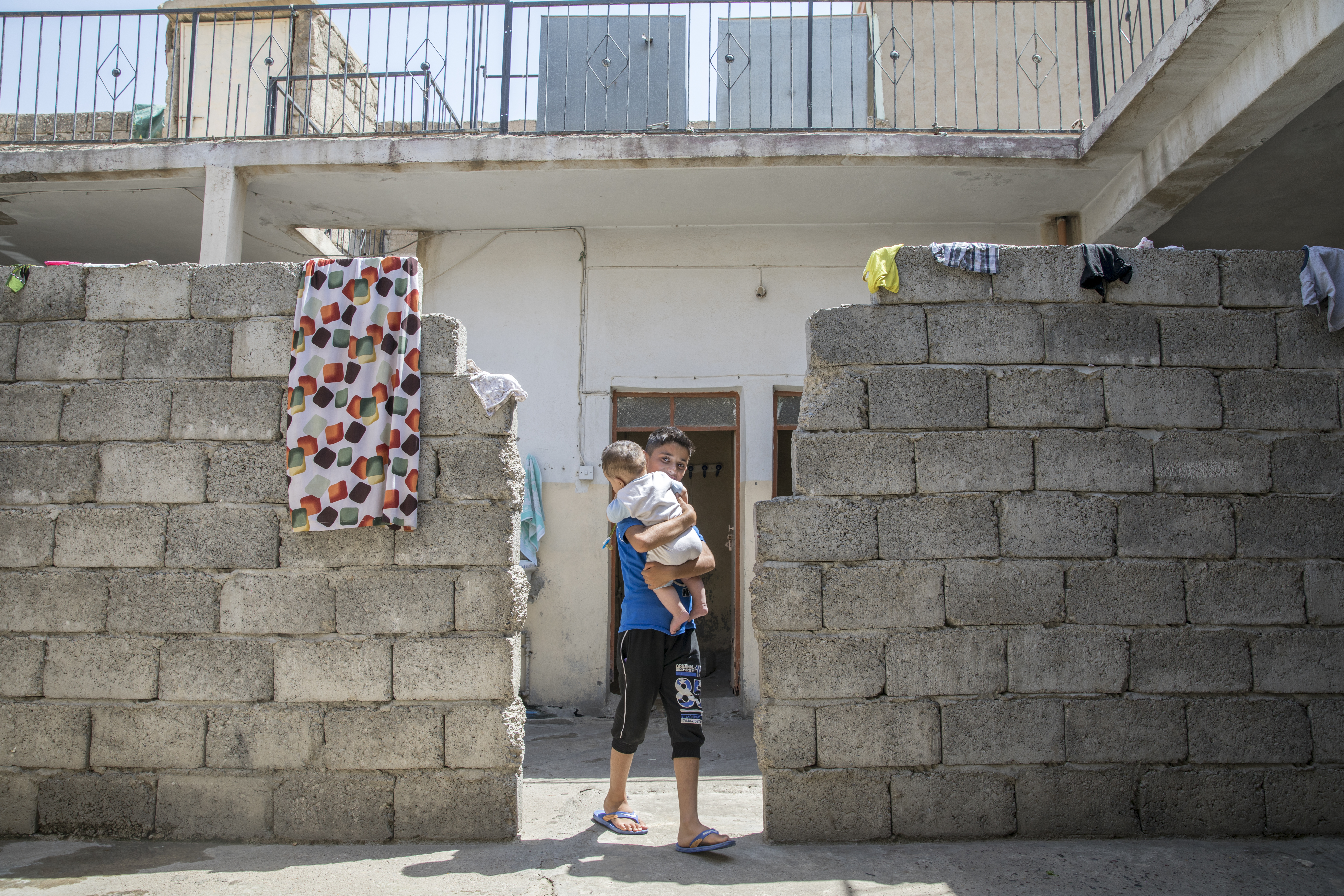 A boy in a cinderblock doorway holding a baby