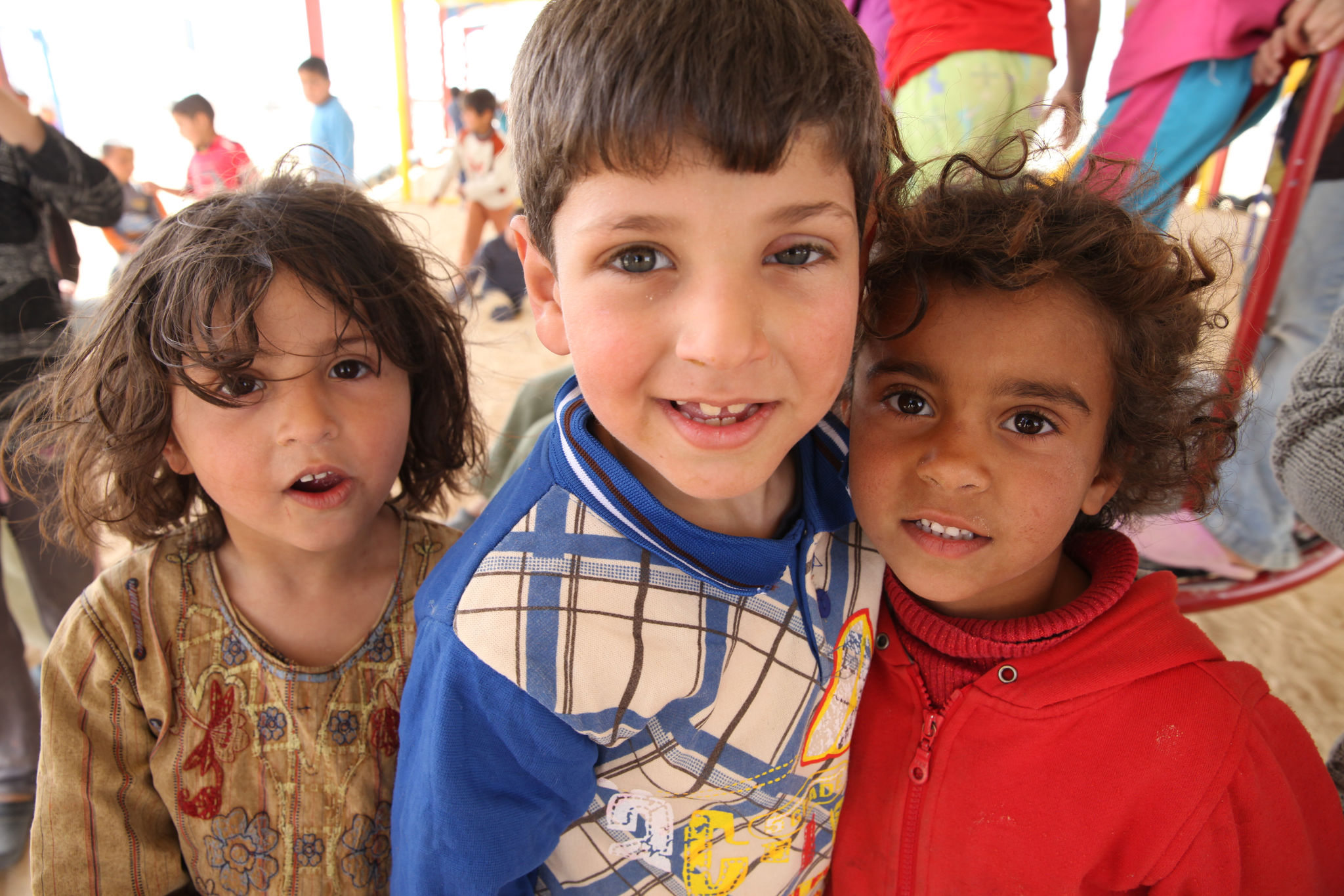 Three young children smile at Zaatari camp.