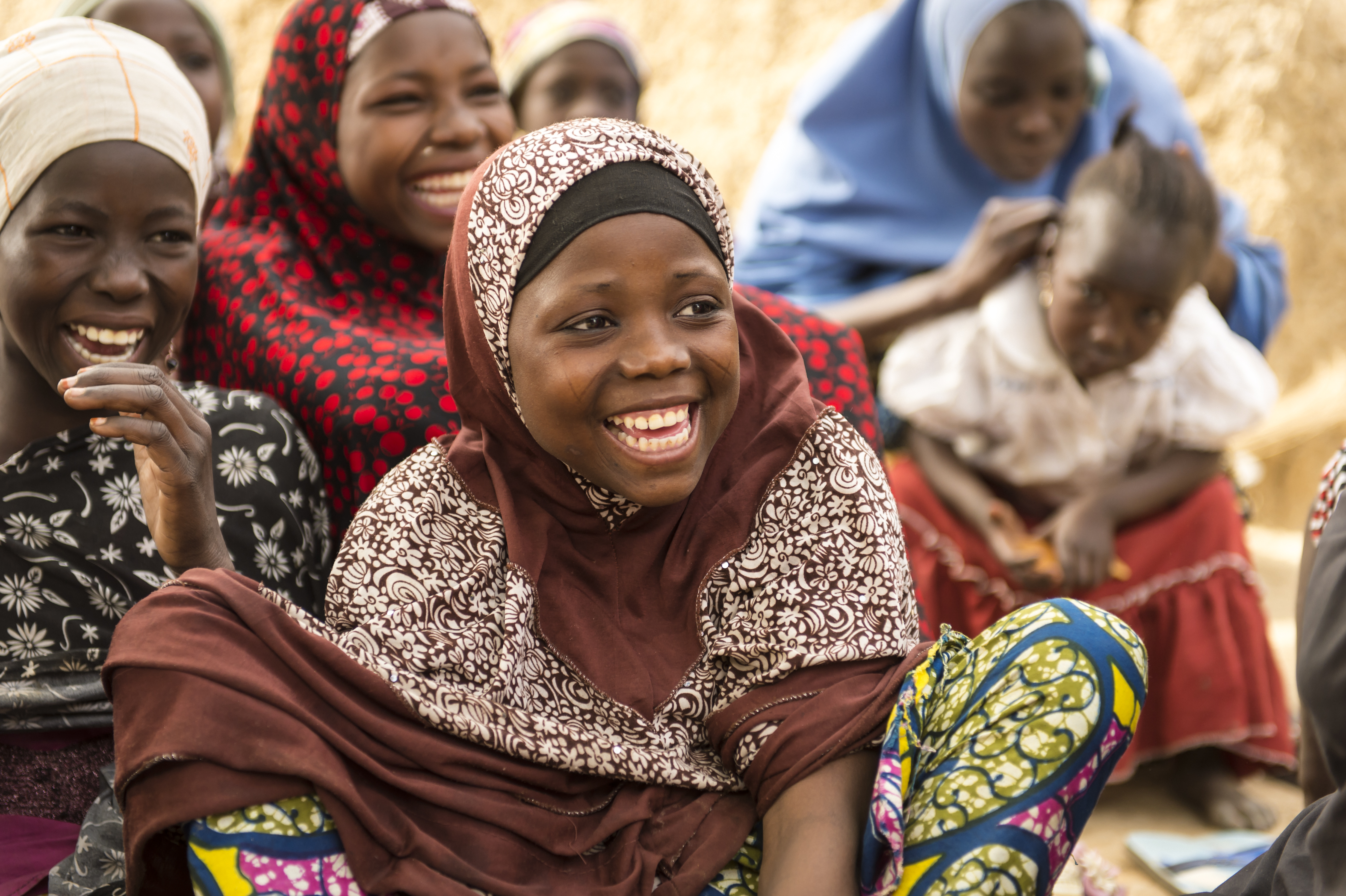 A girl sitting on the ground with other girls nearby, all laughing, in Nigeria