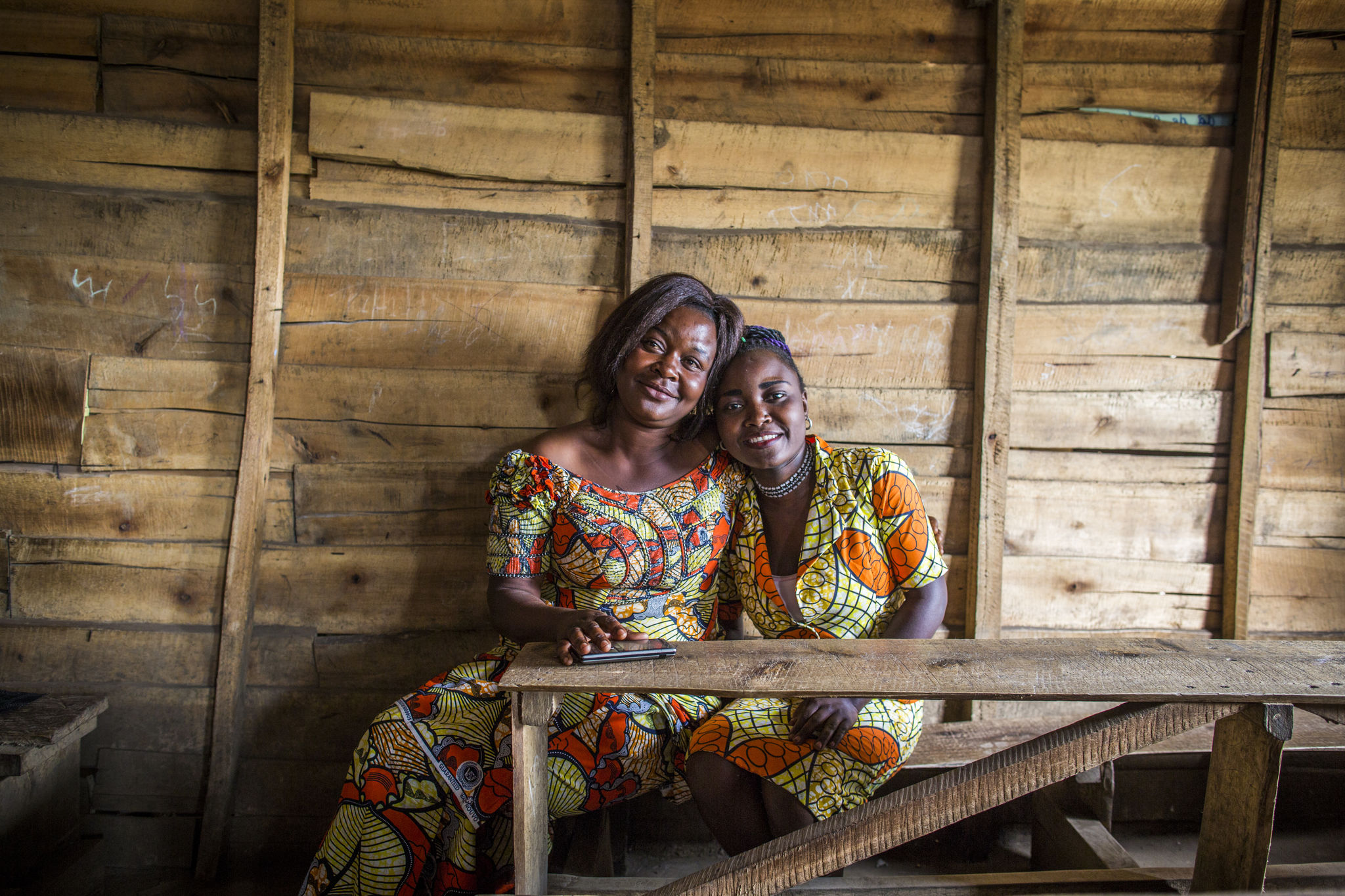 A mother and daughter sit together on a wood bench.