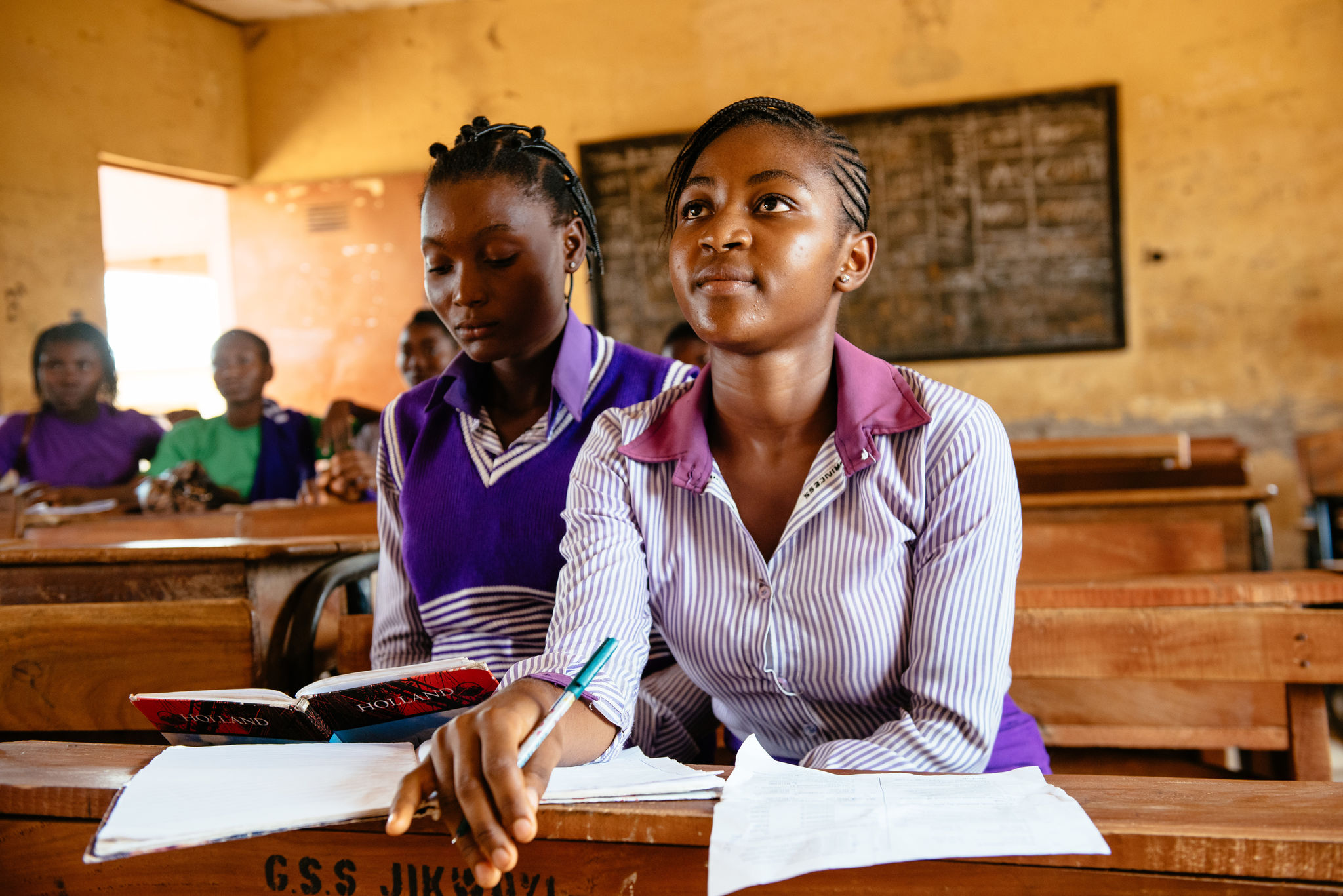 A high school student in Nigeria leans forward in their seat inside a classroom with students. 