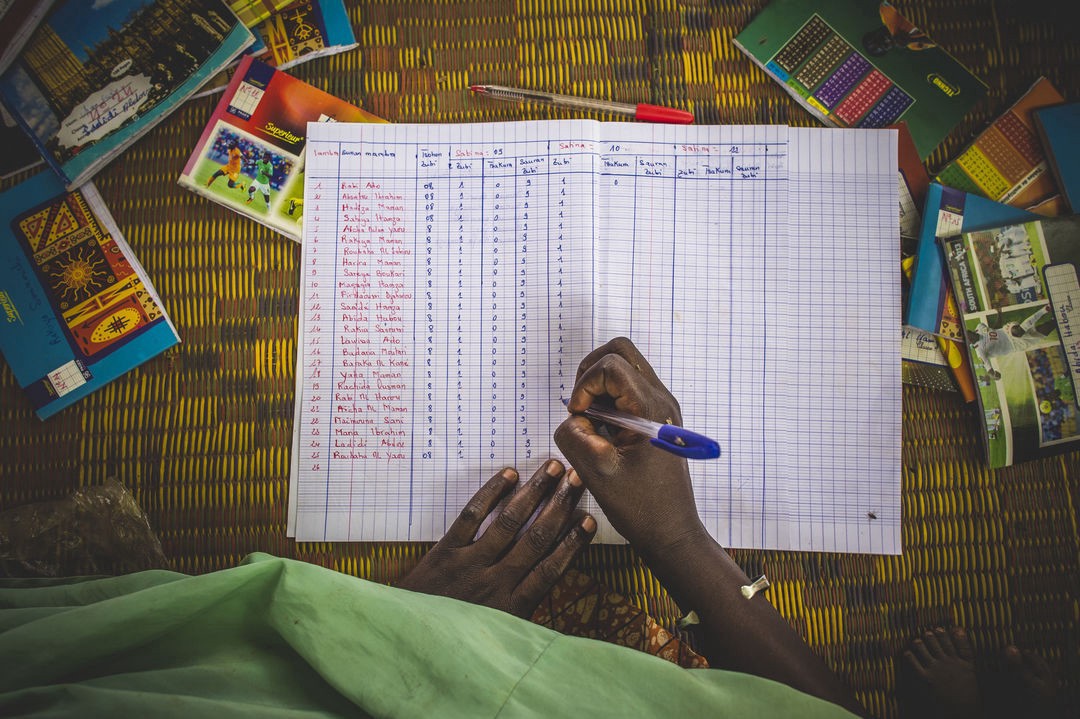 A hand holding a pen marks a paper spreadsheet.