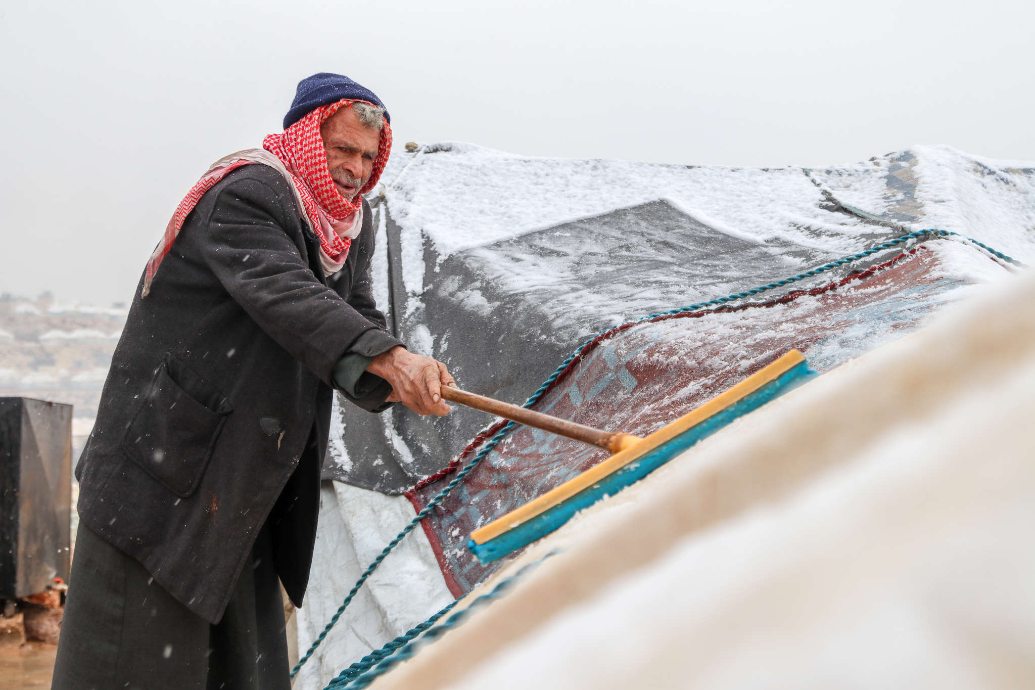 A person uses a broom to try and clear the snow away from their damaged tent.