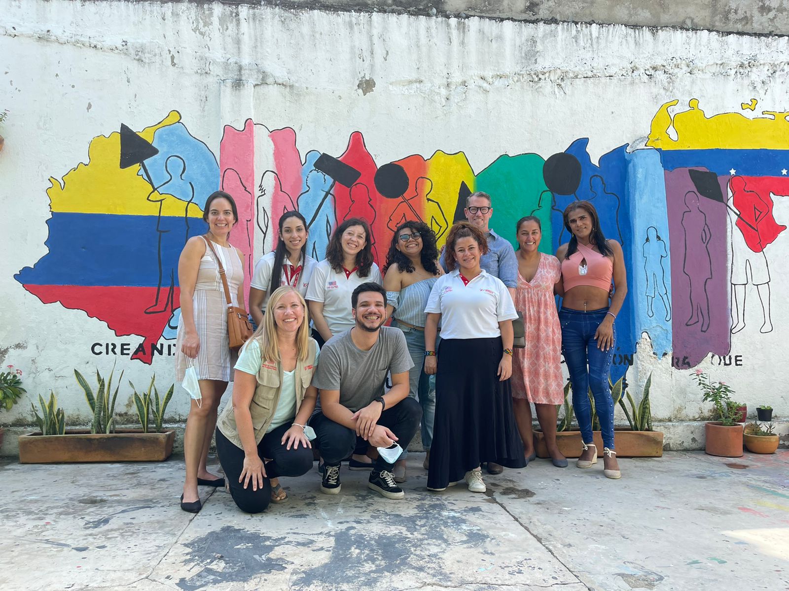 Mercy Corps Colombia team members and participants stand in front of a mural celebrating unity.