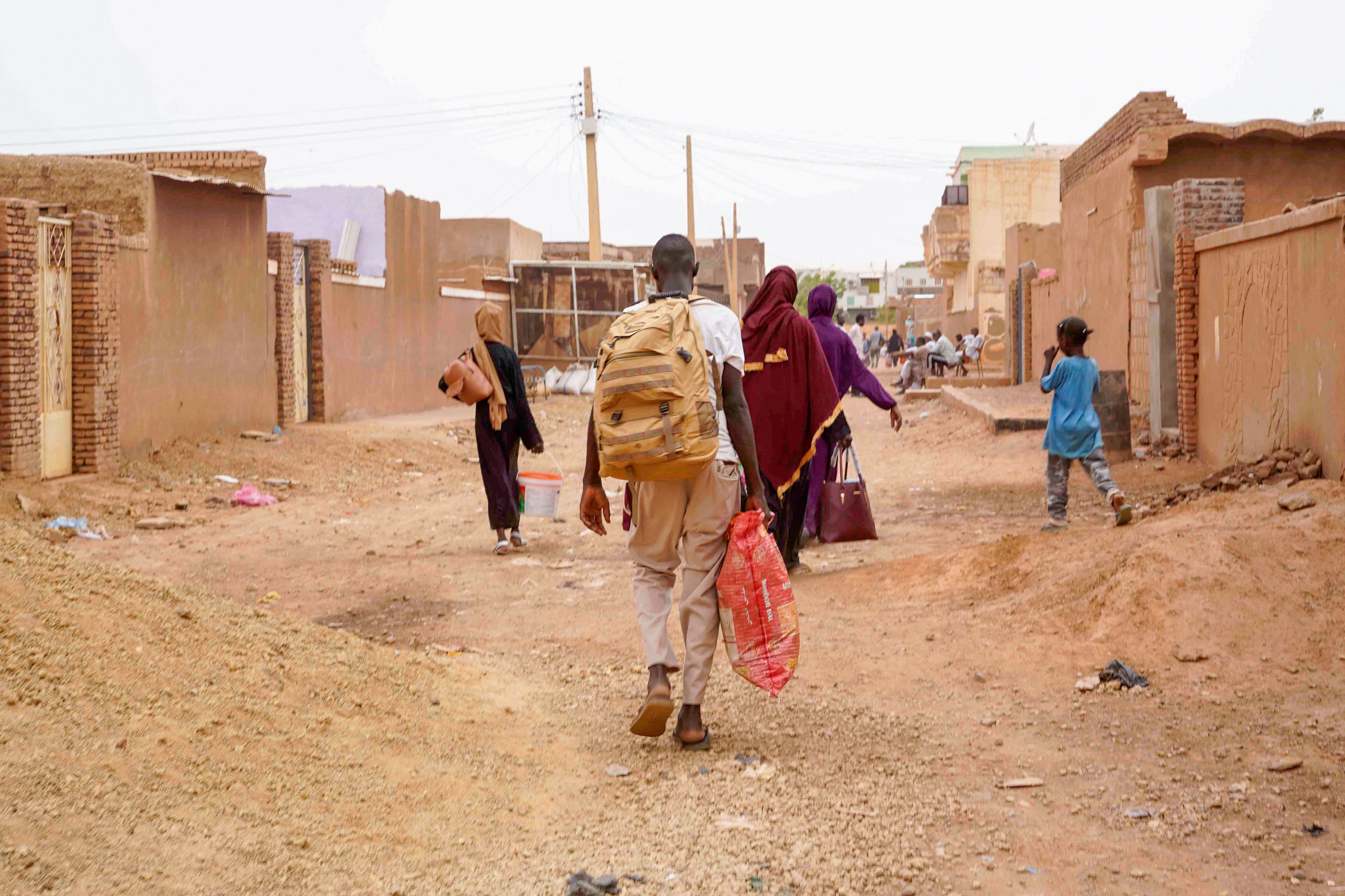 Sudanese community members walk down local street with baggage.