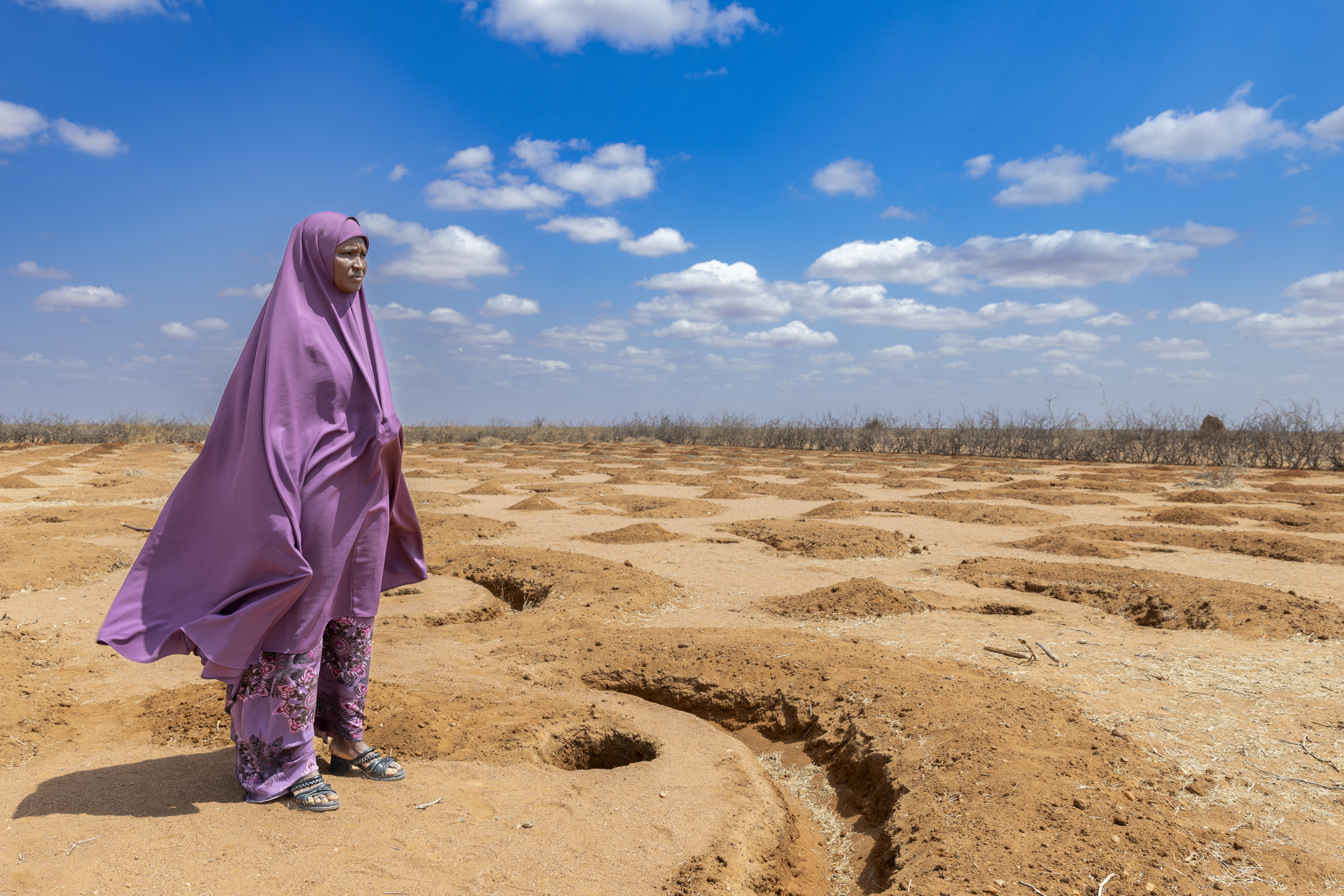 Kenyan woman looks out over arid agricultural land.