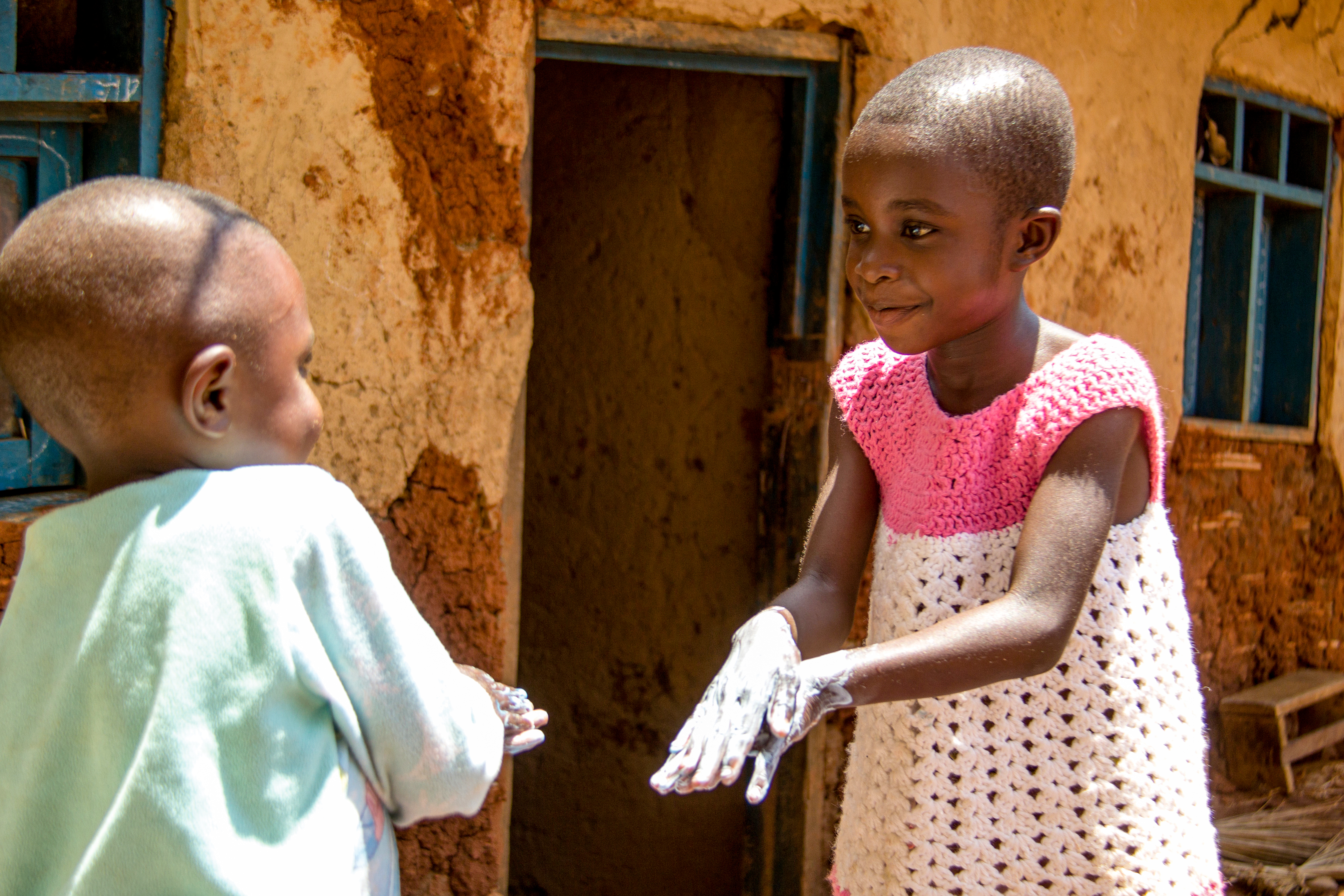 Two children washing their hands outside their home.