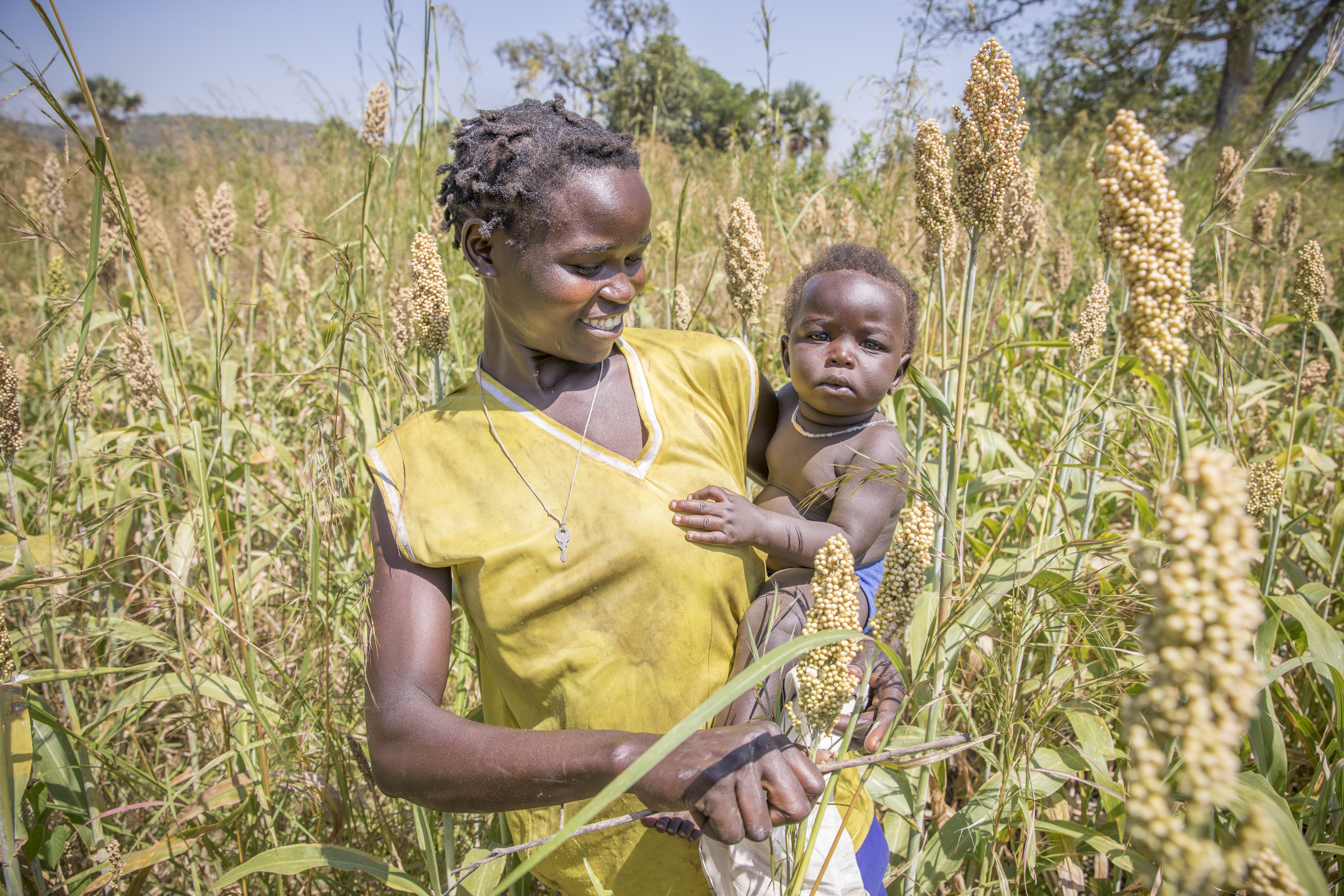 Smiling mother in field in Uganda holding baby