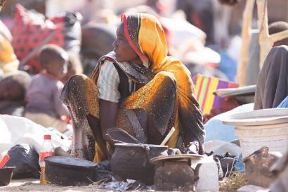 Sudanese woman cooking outside amid refugee group.