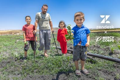 Syrian family standing in the middle of agricultural land, with young boy in foreground offering a bouquet to the camera.