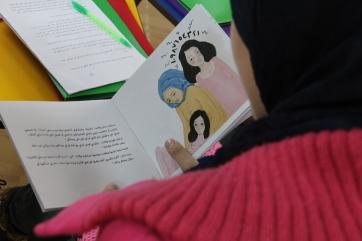A girl reading a book opened to a page with two women and a young girl illustrated on the page