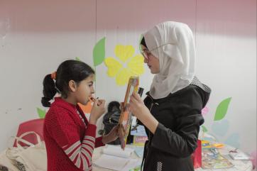 A girl holding up a mirror for another girl who is applying lip gloss