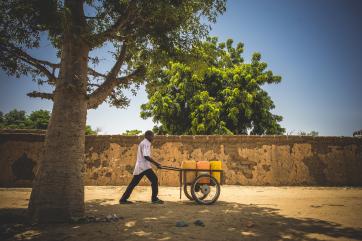 A man pushing yellow water containers on a cart