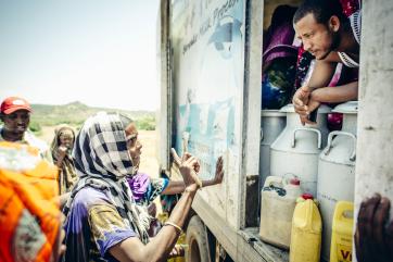 A woman speaks to a man who is leaning out the side of a milk truck in ethiopia