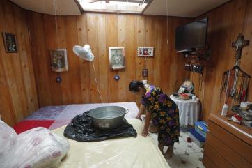 Carmen standing beneath her home's leaking roof with a metal pan in front of her to catch some of the dripping water.