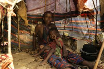 Hadija with a small child on her lap sitting beneath a shelter made of a variety of fabrics