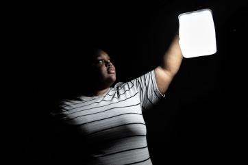 Bahamian woman holds up a solar lantern in the darkness of night.