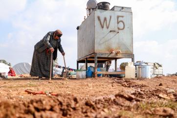Syrian refugee camp water station with woman approaching it.