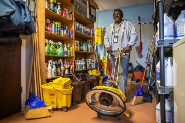 Bahamian man with floor waxer in office storeroom.