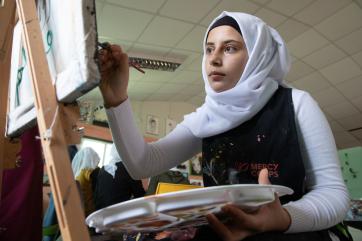 A young person paints while seated at an easel. 