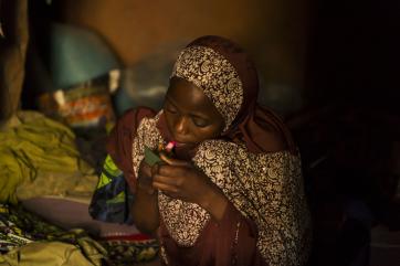 A teenage girl in rural nigeria applies lip makeup. 