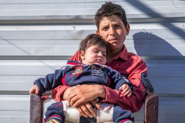 A young participant holds their baby brother in front their family’s caravan in za’atari, jordan.