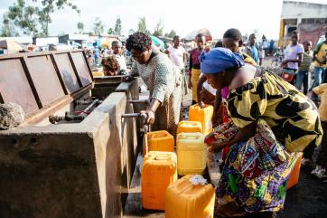 A group of people fill water vessels.