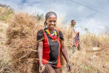An adult smiles for the camera while cutting grass on a hill in ethiopia.