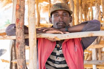 An adult leans on a wooden structure while resting their head on their hands.