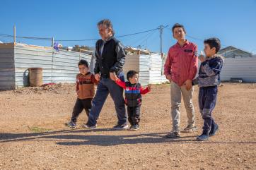 An adult walks through za’atari refugee camp with their four sons in jordan.
