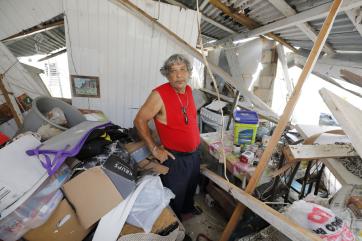 An adult stands in room littered with debris from a hurricane.   