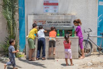 A group of children fill bottles at a water station.