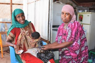Two ethiopian women seated with one of the women holding a baby