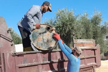 A man hoisting a tank to a man standing on a flat bed truck