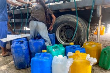 Palestine filling up jerrycans of water from truck parked in gaza street.