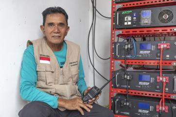 Indonesian man with hand radio and broadcasting equipment intended for use during emergency moments.
