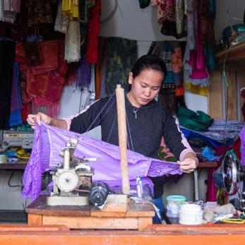 A view through a window into a shop with a woman working with fabrics.