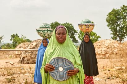 Three nigerian woman in traditional dress; two with balanced loads on their heads.