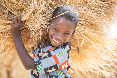 A young boy with a bright smile carrying grass