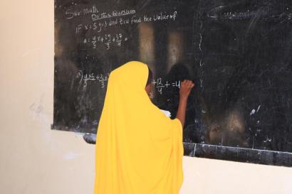 Somalian woman at chalkboard working on a math problem.