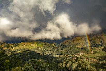 A rainbow appears in clouds forming over hills and mountains in timor-leste.