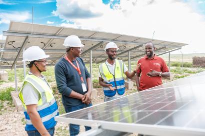 Four people wearing safety gear inspect a solar panel.