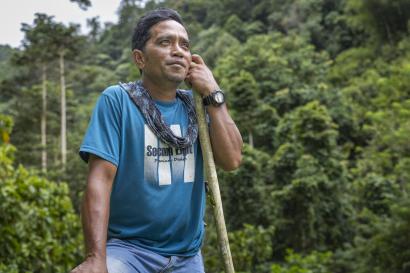 Indonesian man smiling, leaning on an agricultural implement outside.